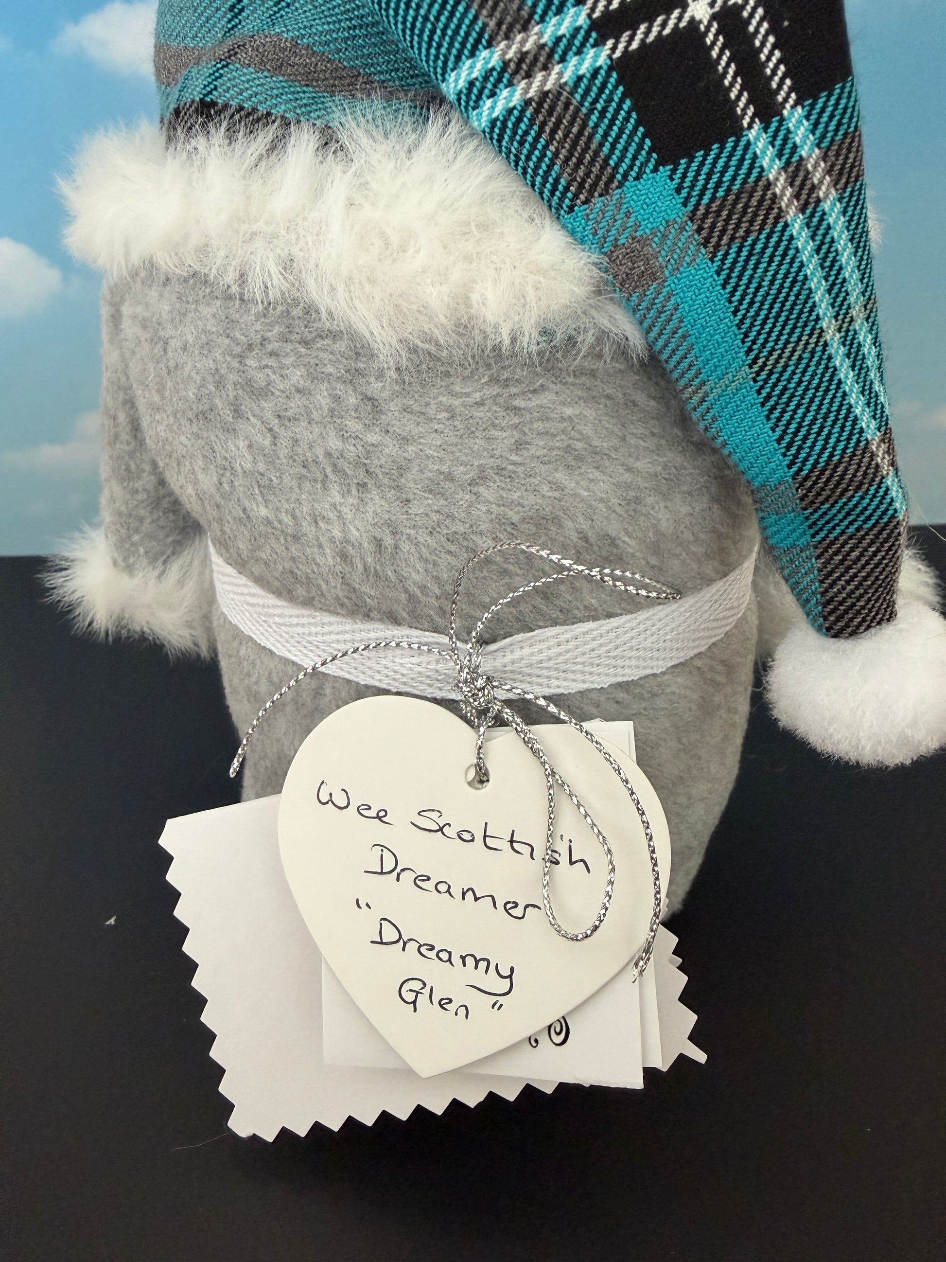A rear view close-up of a  Gnome wearing a teal, black, and white plaid hat with white pom-pom handmade by Northern Nomes.
