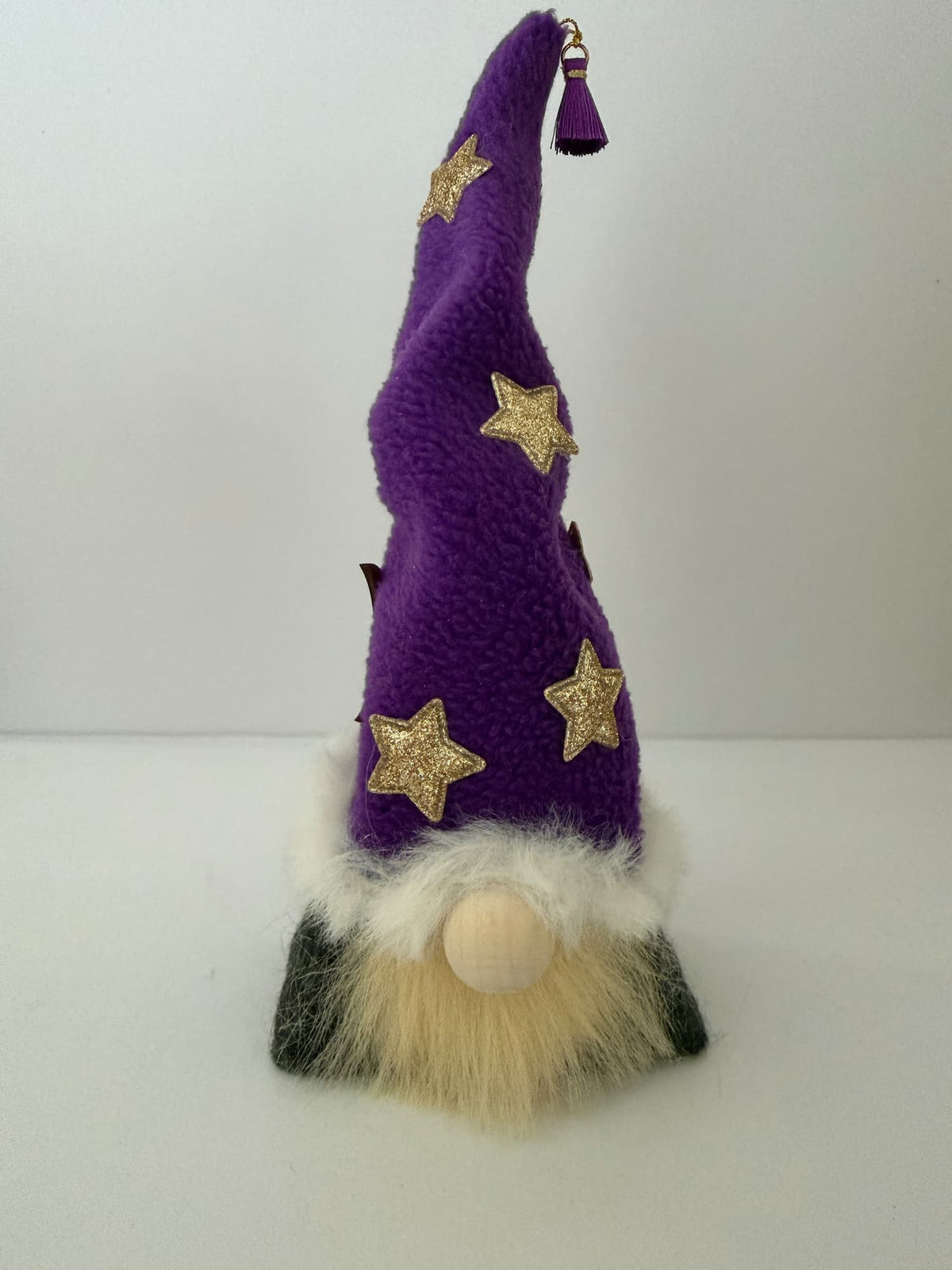 A handmade plush wizard gnome decoration with a tall purple hat adorned with gold glitter stars, a fluffy white and beige beard, and dark gray shoes, photographed against a plain white background. Part of the Northern Nomes collection of gnomes and gonks.