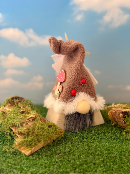 A handmade mushroom styled gnome ornament with a brown fleece hat, white faux fur trim, small wooden nose and a black faux fur beard. The hat features two red ladybird embellishments. Made by Northern Nomes and part of the Mosswood collection.