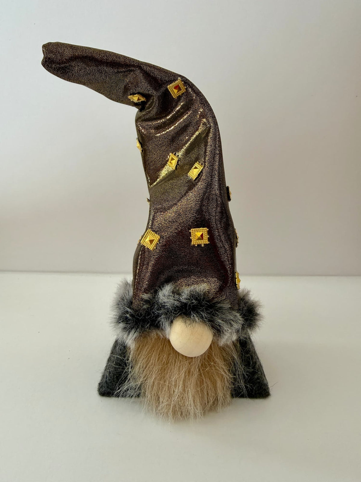 A small wizard gnome figurine with a tall metallic bronze hat decorated with gold diamond shapes, a fluffy beige beard, and a grey faux-fur trim, standing on a white background. Handmade by Northern Nomes.