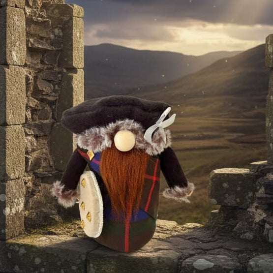 A small gnome figurine with a long ginger beard, black hat, and red-and-brown Fraser tartan outfit stands on a stone ledge inside a ruined stone structure, looking out toward a dramatic mountain landscape under a cloudy sky. Handmade Jacobite Gnome by Northern Nomes.