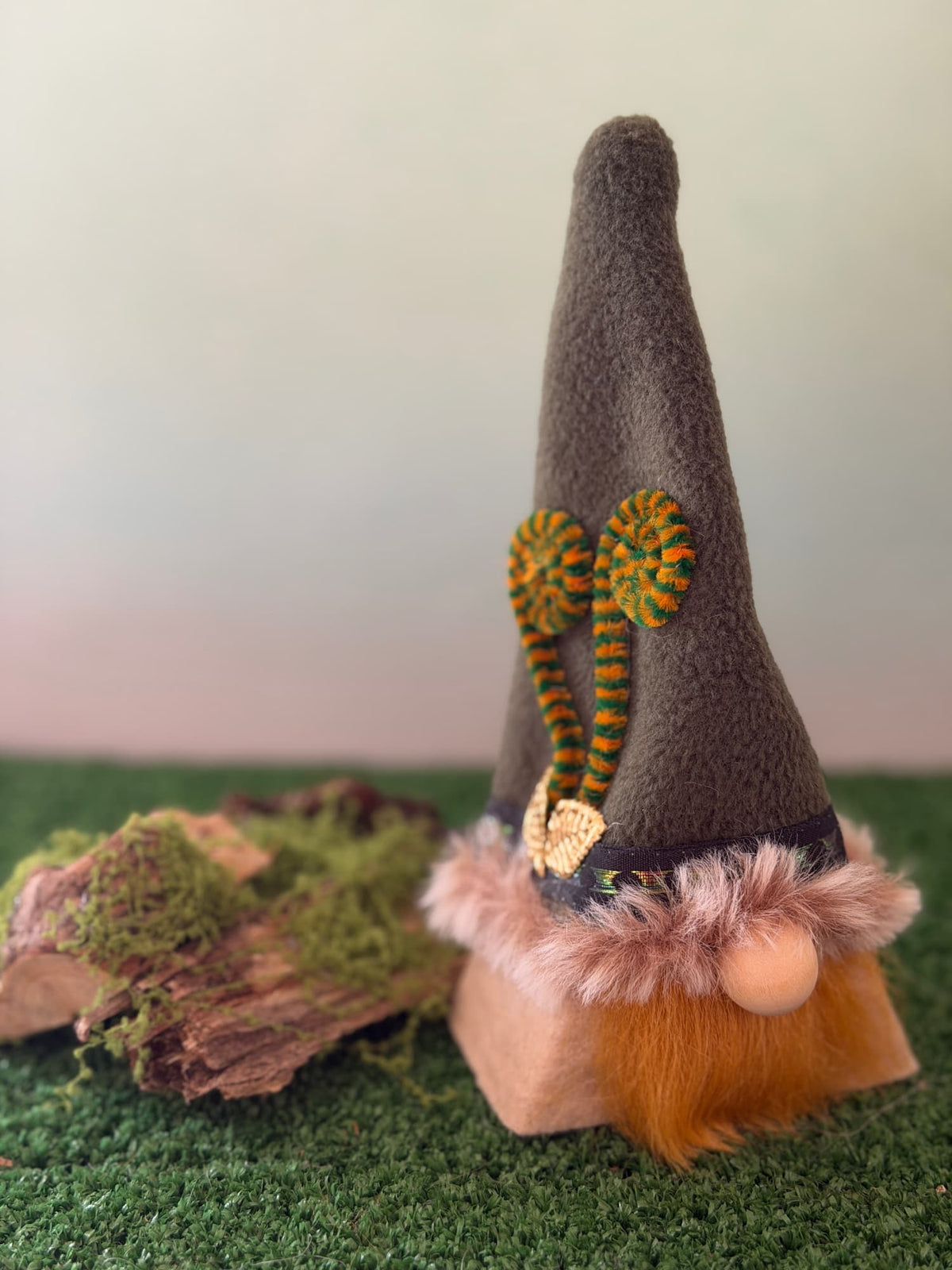 Handmade gonk figure by Northern Nomes. Tall greenish fleece hat with faux fur trim and 2 gold leaves.Ginger beard and wooden bead nose, with a grassy forest background.