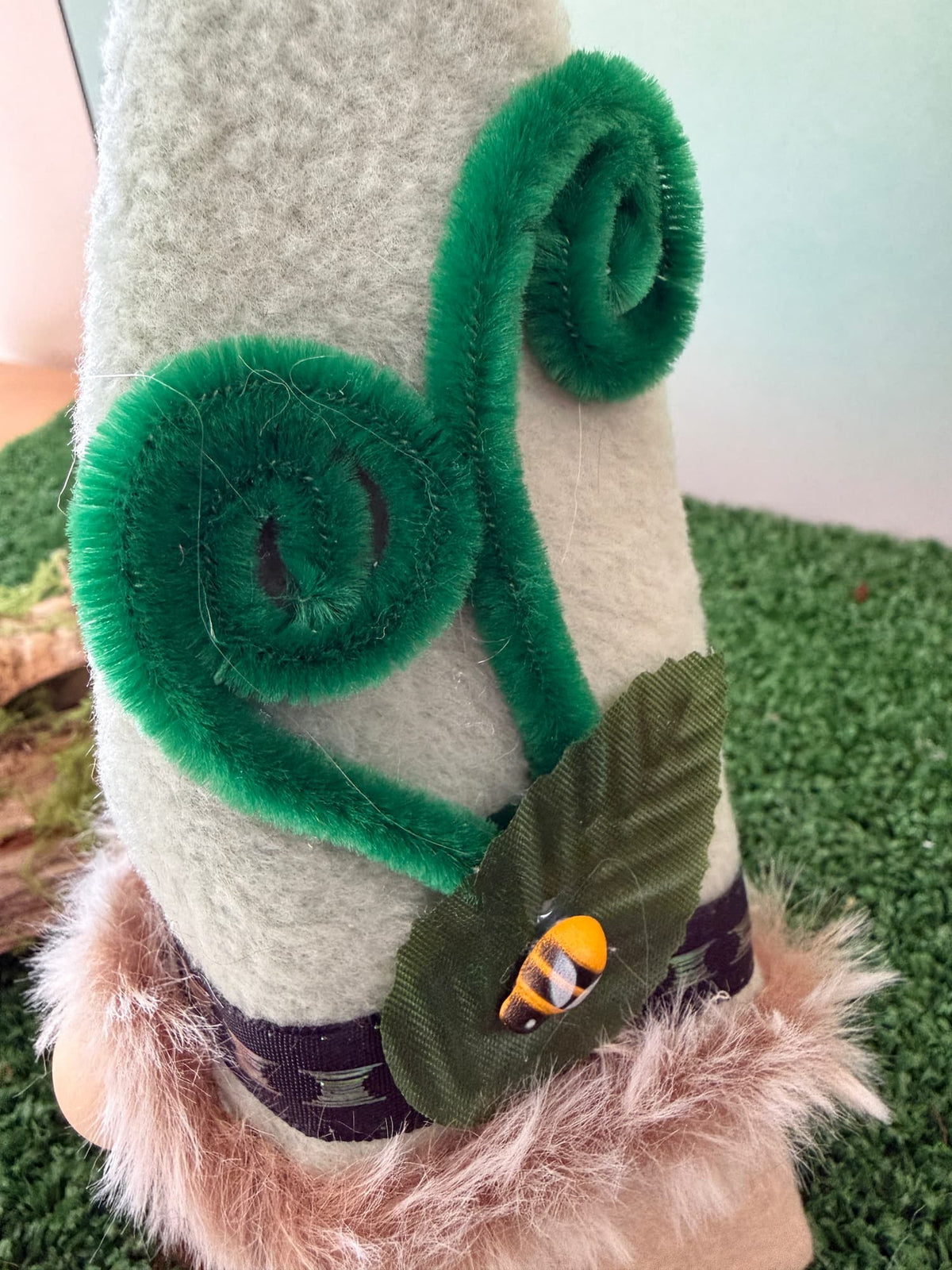 Close up of a handmade gnome hat with two green fern like swirls, a green leaf and a tiny bee resting on the leaf.