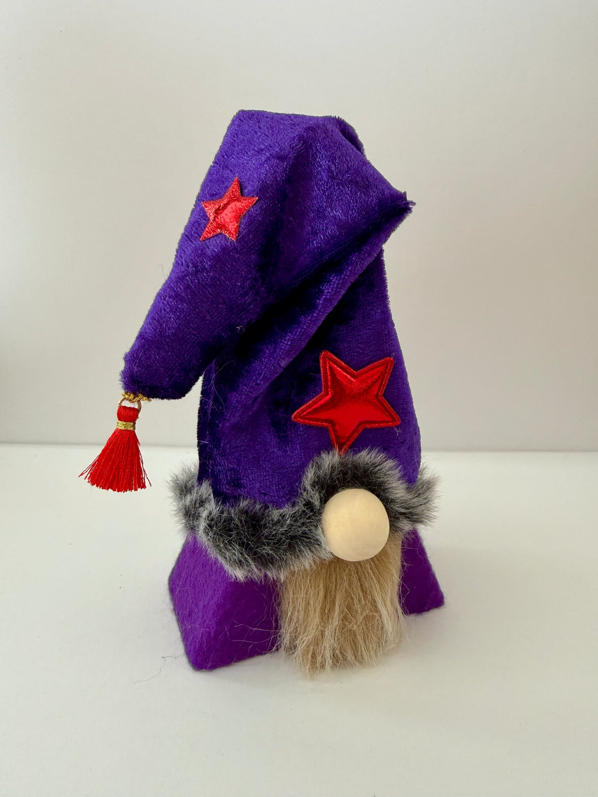 A small wizard gnome figurine wearing a purple pointed hat with red star appliqués and a fluffy cream beard, standing on a white background. Handmade by Northern Nomes.