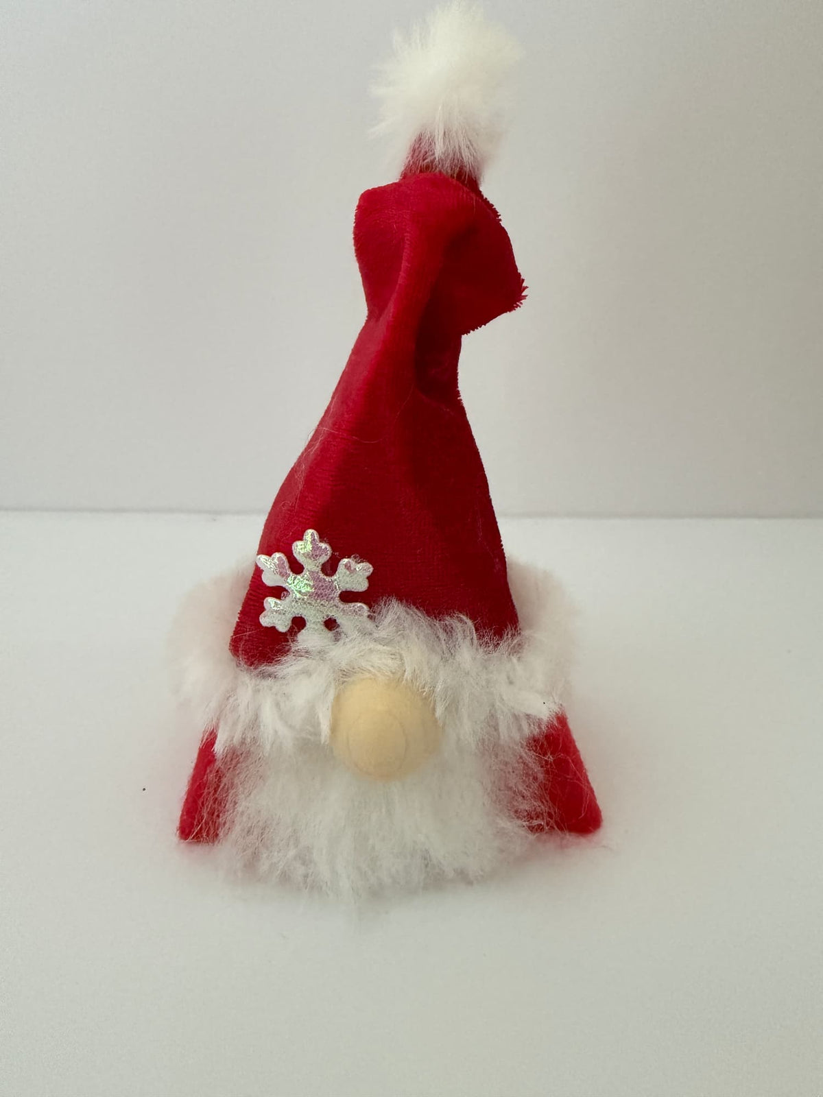 A handmade small decorative Santa Christmas gnome figure wearing a red hat with white faux fur trim, a white pom-pom on top, and a silver snowflake ornament on the side. From the festive folk collection by Northern Nomes.