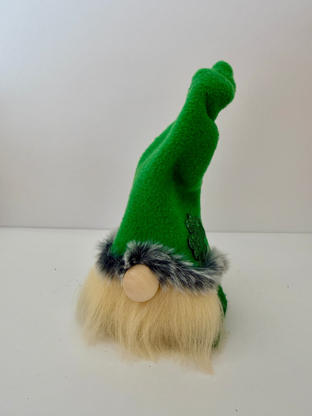 A handmade lucky Leprechaun green gnome figurine with a tall pointed hat, fluffy cream beard, gray faux-fur trim, and a round wooden nose, photographed against a plain white background. Made by Northern Nomes and part of the Cloverhill Folk collection.