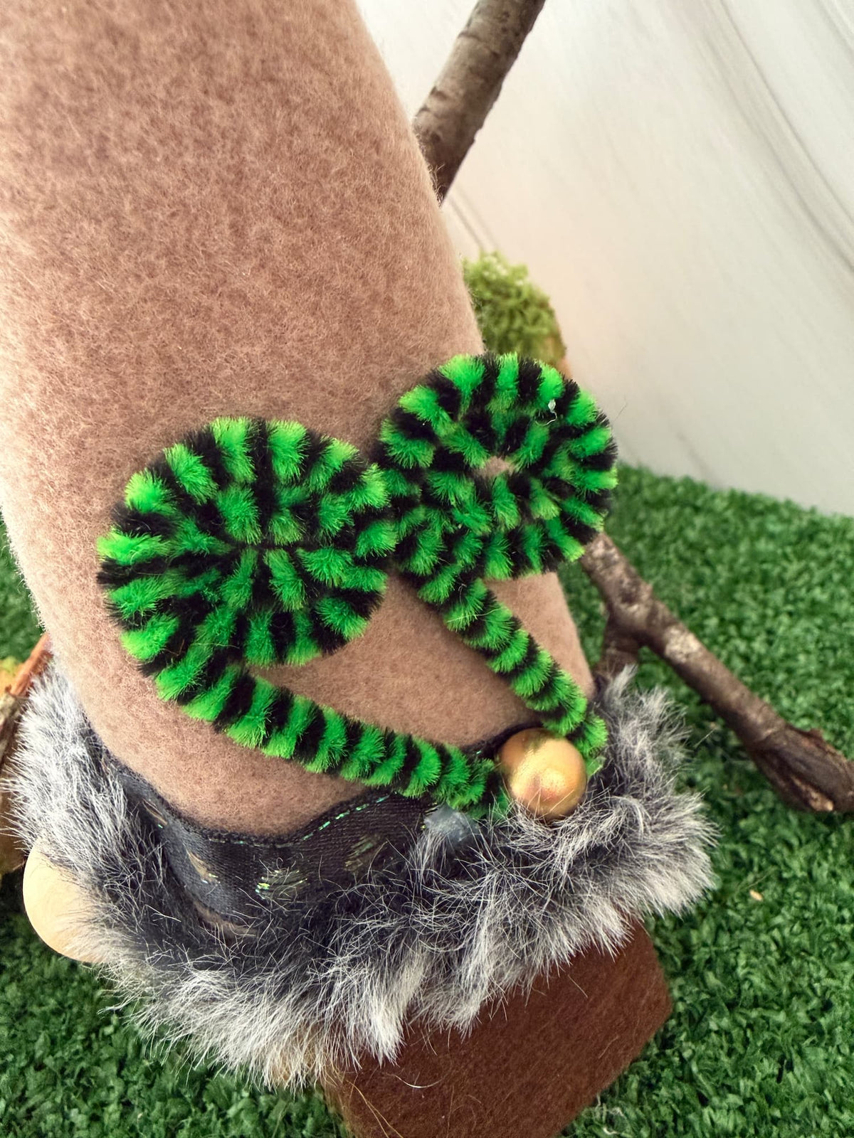 A close-up of a brown body gonk with a fleece hat and a gray faux-fur trim. There is a green and black styled fern embellishment.
