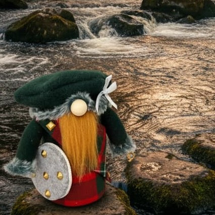 Handmade by Northern Nomes a Jacobite gnome figurine with a green hat, long ginger beard, and MacGregor tartan Kilt and Plaid clothing, stands on a mossy rock by a flowing forest stream at sunset.