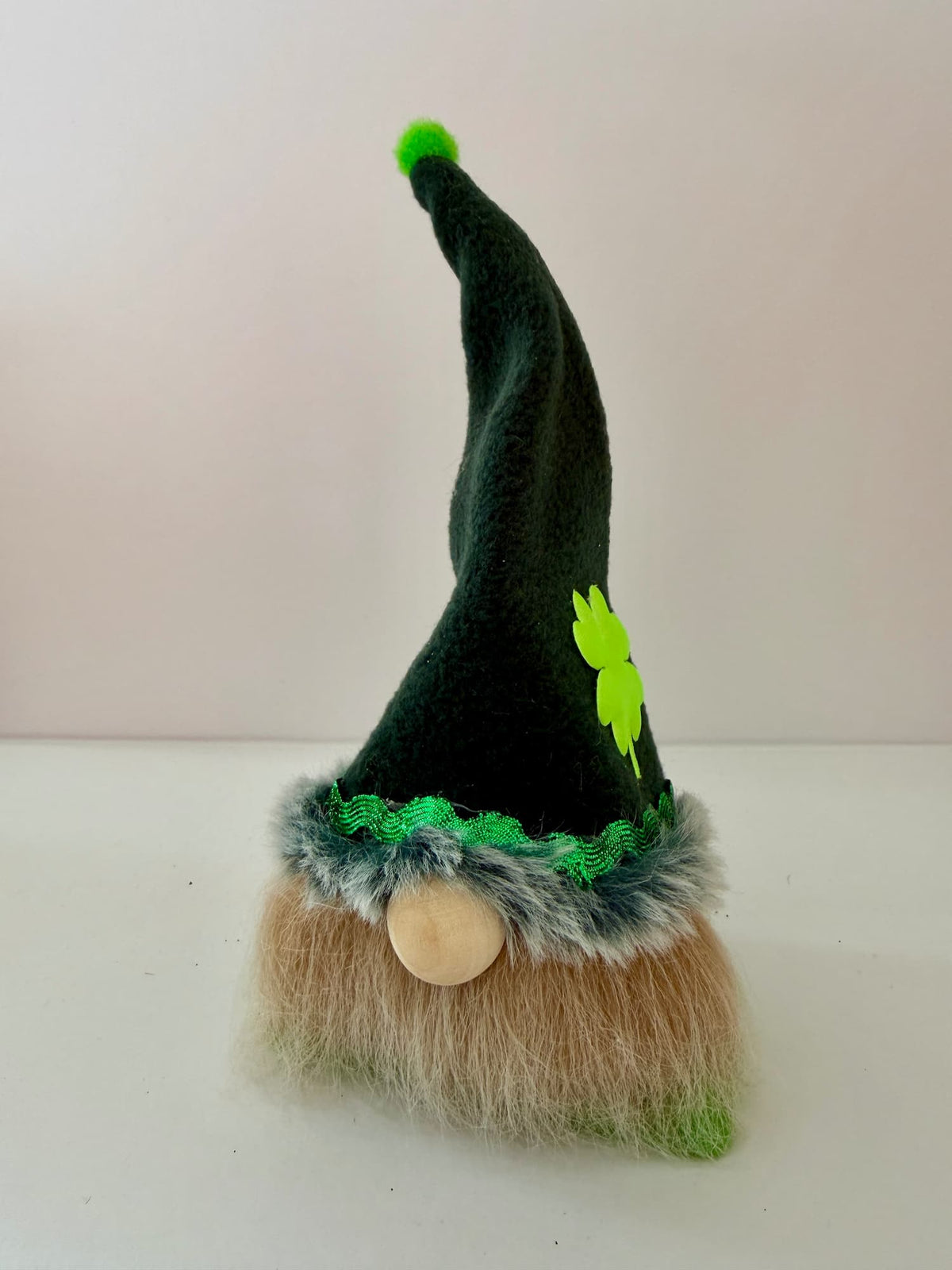 A small Lucky Leprechaun gnome decoration with a tall dark green pointed hat, bright green shamrock accent, faux fur trim, and a beige shaggy beard on a plain light background. Handmade by Northern Nomes and part of the Cloverhill Folk collection.